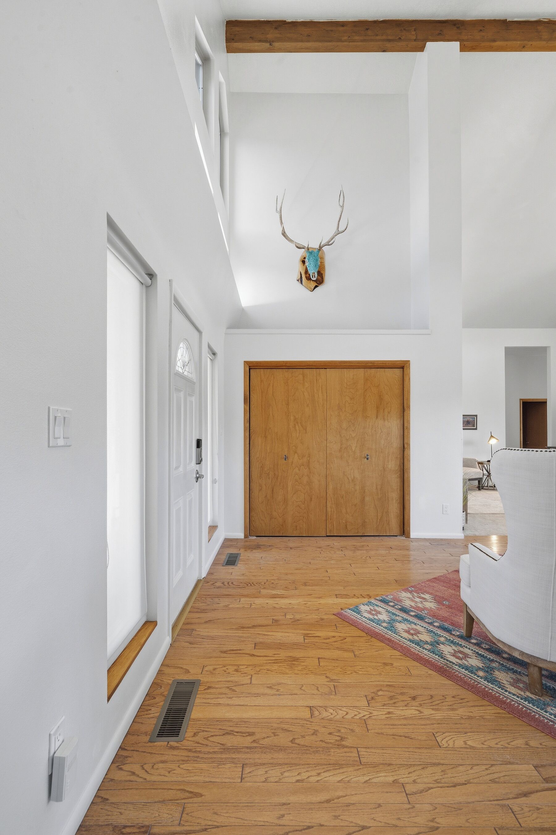 Un couloir doté d’un plancher en bois, d’une grande porte en bois et d’une tête de cerf fixée au mur.