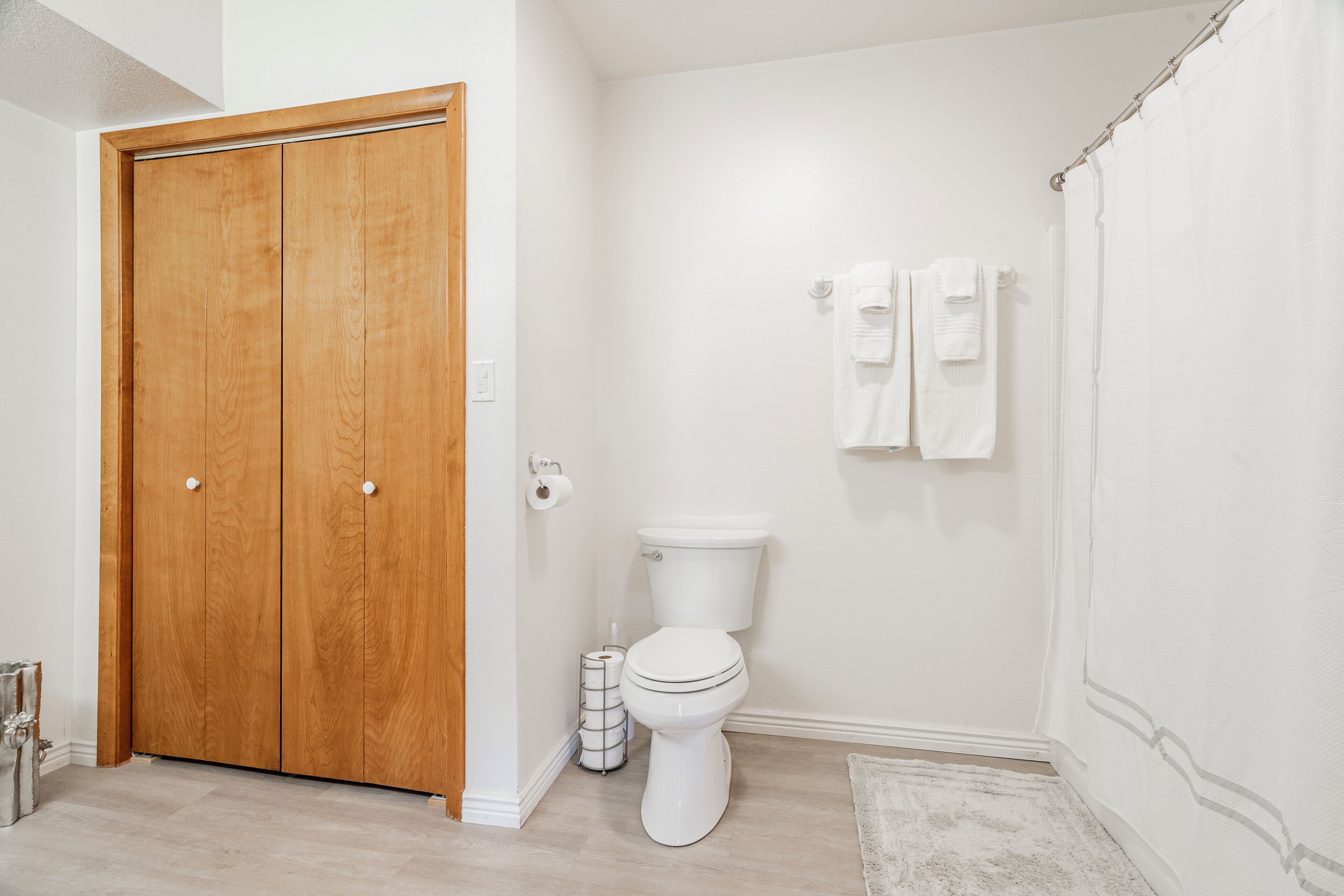 Une salle de bain avec une porte en bois, des toilettes blanches et un rideau de douche.