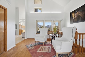 A spacious living room with a high ceiling, a large window with a mountain view, a dining area with a table and chairs, and a staircase with wooden railings. - Starry Nites Ranch (New Harmony)