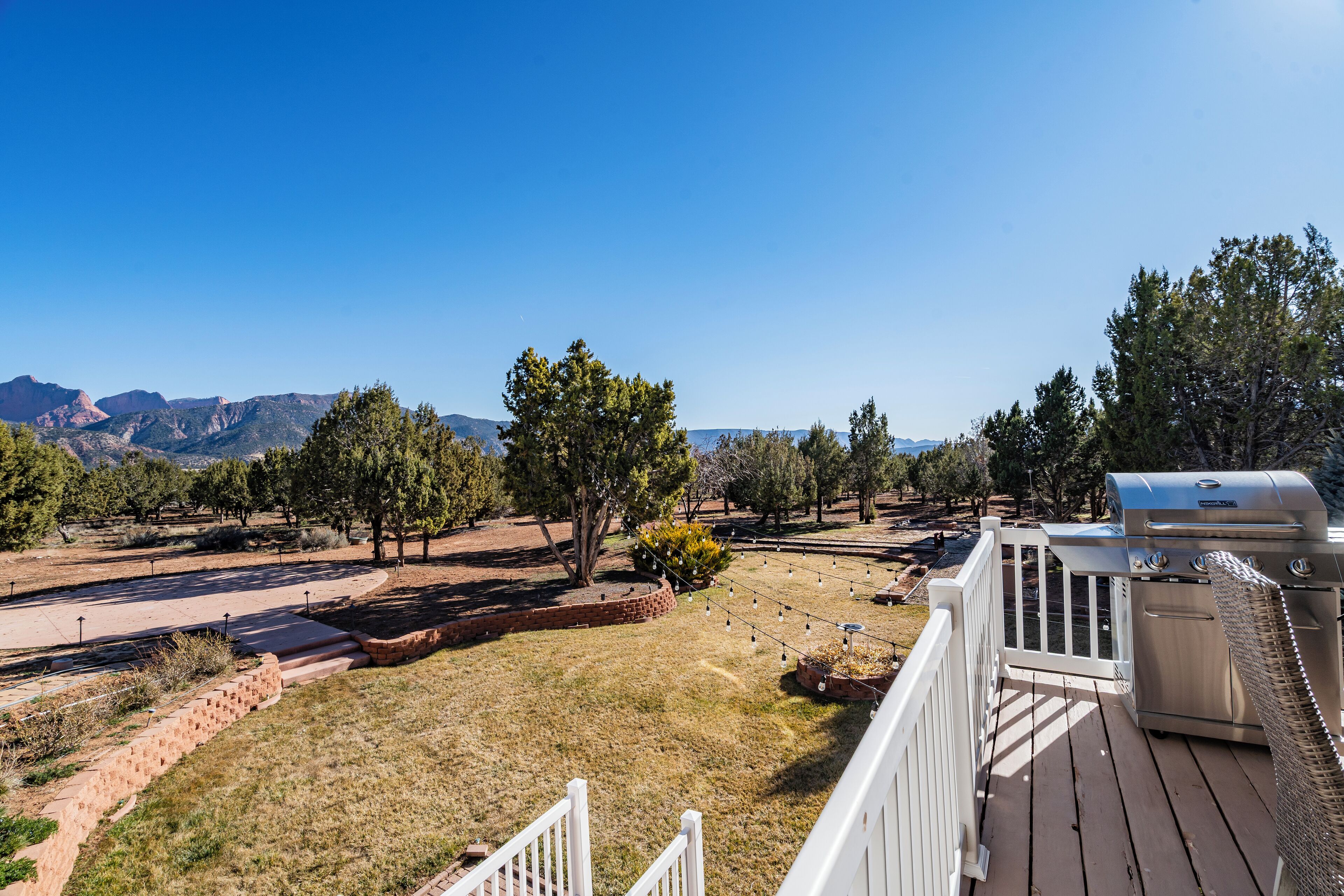 A deck with a barbecue grill, a white fence, and a view of mountains.