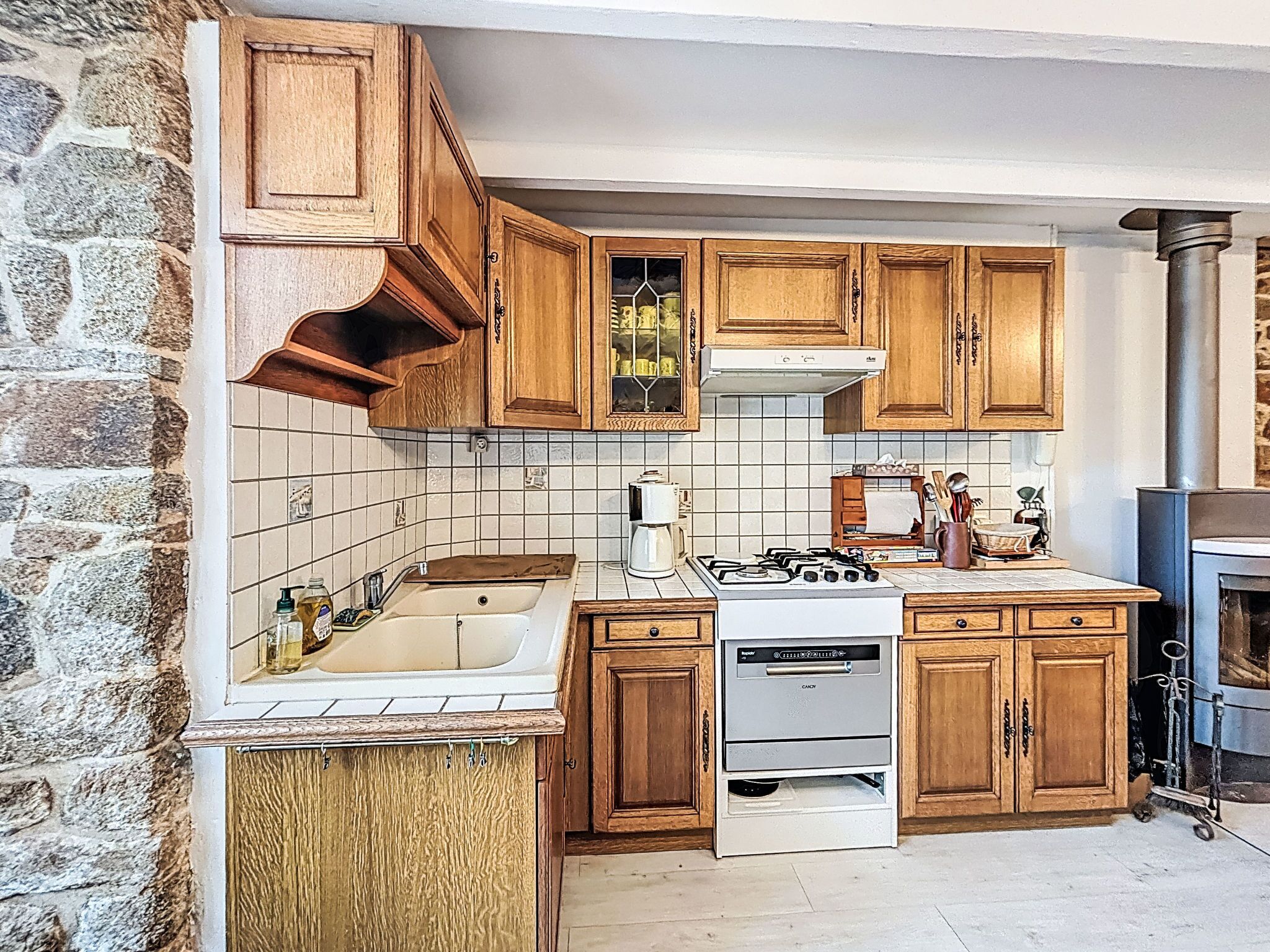 A kitchen with wooden cabinets, a stove, a dishwasher, and a stone wall.