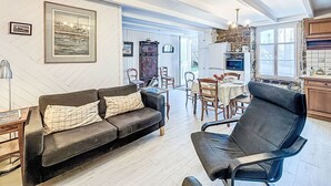Un salon chaleureux avec un canapé, des fauteuils, une table à manger et un coin cuisine doté d’un mur en pierre et de meubles de rangement en bois.