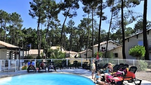 Zona de piscina con sillas de descanso y una alberca rodeada de árboles altos.