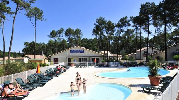 Zona de piscina con sillas de descanso, un edificio con un letrero y árboles al fondo.
