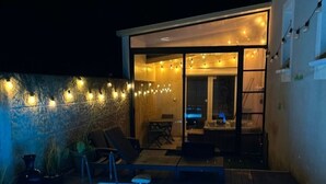 Un espace piscine doté d’une zone couverte, de chaises longues et de guirlandes lumineuses.