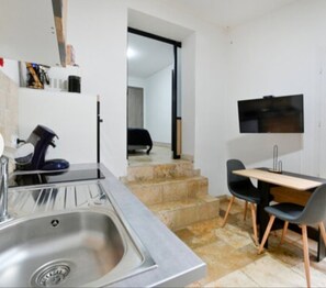 A compact kitchen with a sink, a small table, and chairs, and a TV mounted on the wall.
