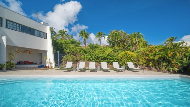 A clear blue pool with lounge chairs and a white building with large windows. - Villa Lala, a chic getaway with pool and sea view (Case-Pilote)