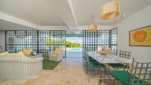 Un vaste espace de vie comprenant une table à manger, des chaises et un canapé. Une paroi vitrée offre une vue sur la piscine.