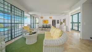 A spacious living area with wicker furniture, a green rug, and large windows offering ocean views. - Villa Lala, a chic getaway with pool and sea view (Case-Pilote)