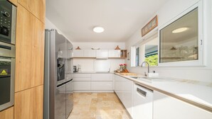 A modern kitchen with white cabinetry, stainless steel appliances, and a large window providing natural light. - Villa Lala, a chic getaway with pool and sea view (Case-Pilote)