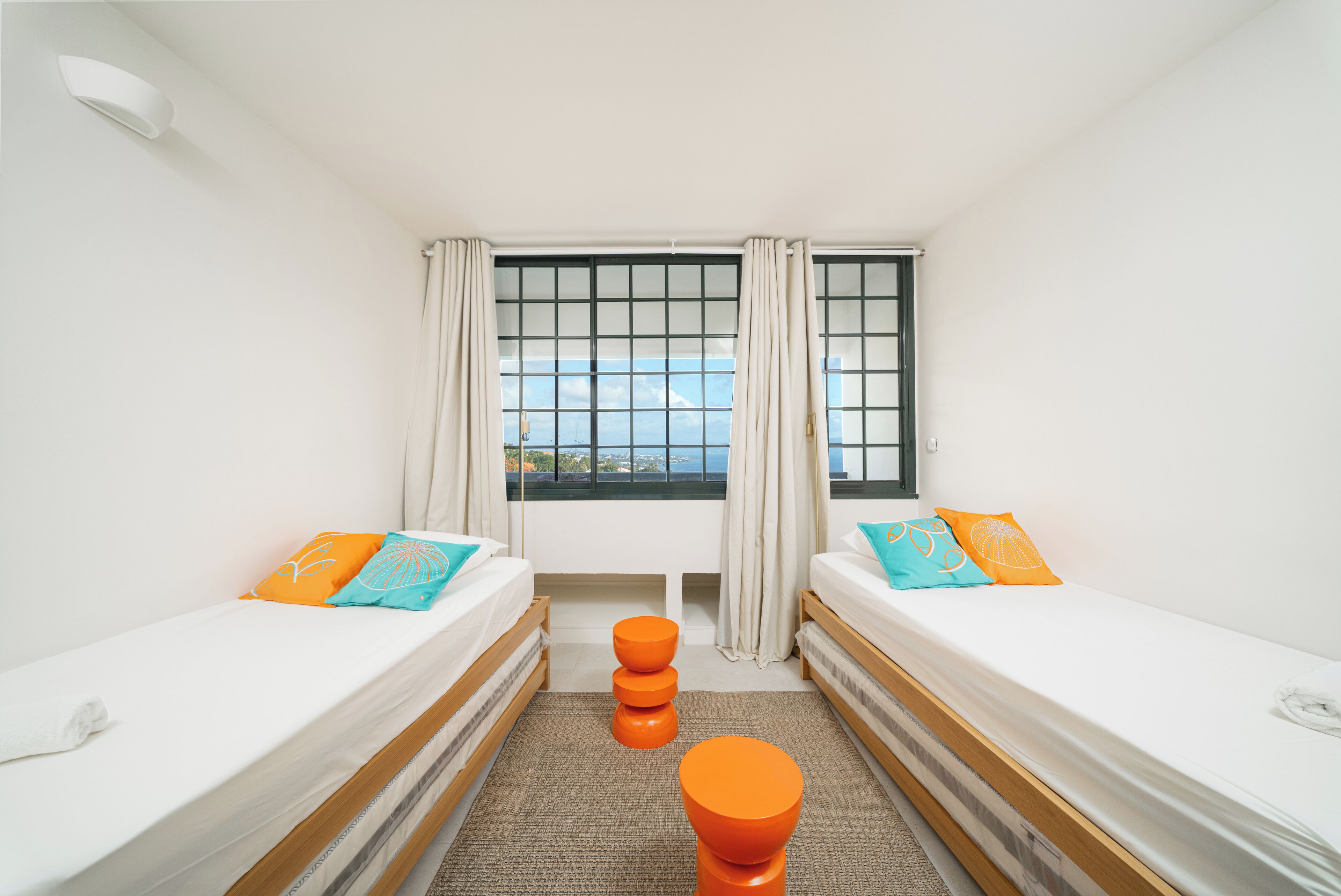 Una habitació amb dos llits, una finestra amb cortines, i vista al mar.