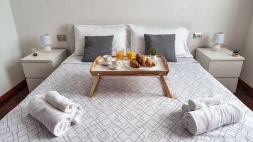 Un letto rifatto con cura e un vassoio con prodotti per la colazione, tra cui croissant e succo d'arancia, in una camera d'albergo dal design semplice ed essenziale.