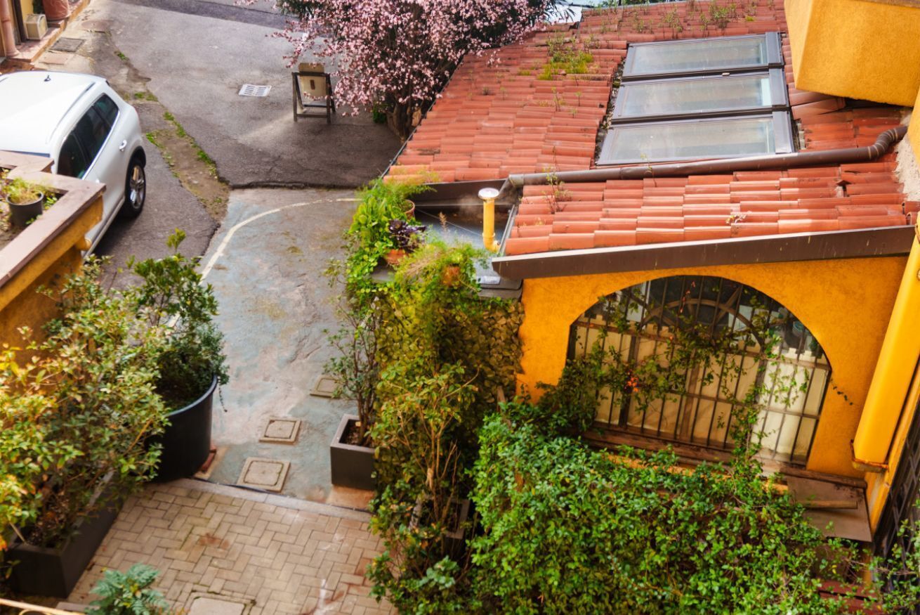 Un cortile con tetto in tegole rosse, un muro giallo e un cancello in metallo nero.