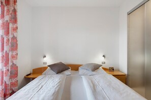 Ein Doppelbett mit zwei Kissen, ein Nachttisch aus Holz, eine Fernbedienung und eine Wandleuchte.