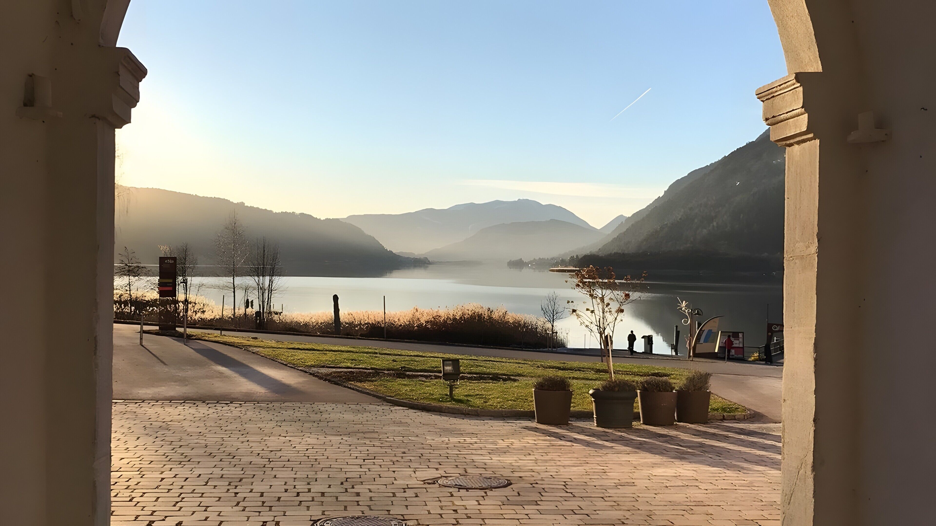 Een geplaveid pad dat naar een meer leidt, met bergen op de achtergrond.