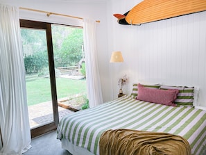 Un dormitorio con cama, ventana con cortinas, lámpara y vistas al exterior.