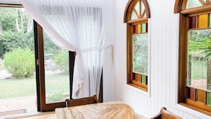 Un espace repas avec une grande table en bois, des murs recouverts de panneaux blancs et des fenêtres en arc surmontées de vitraux.