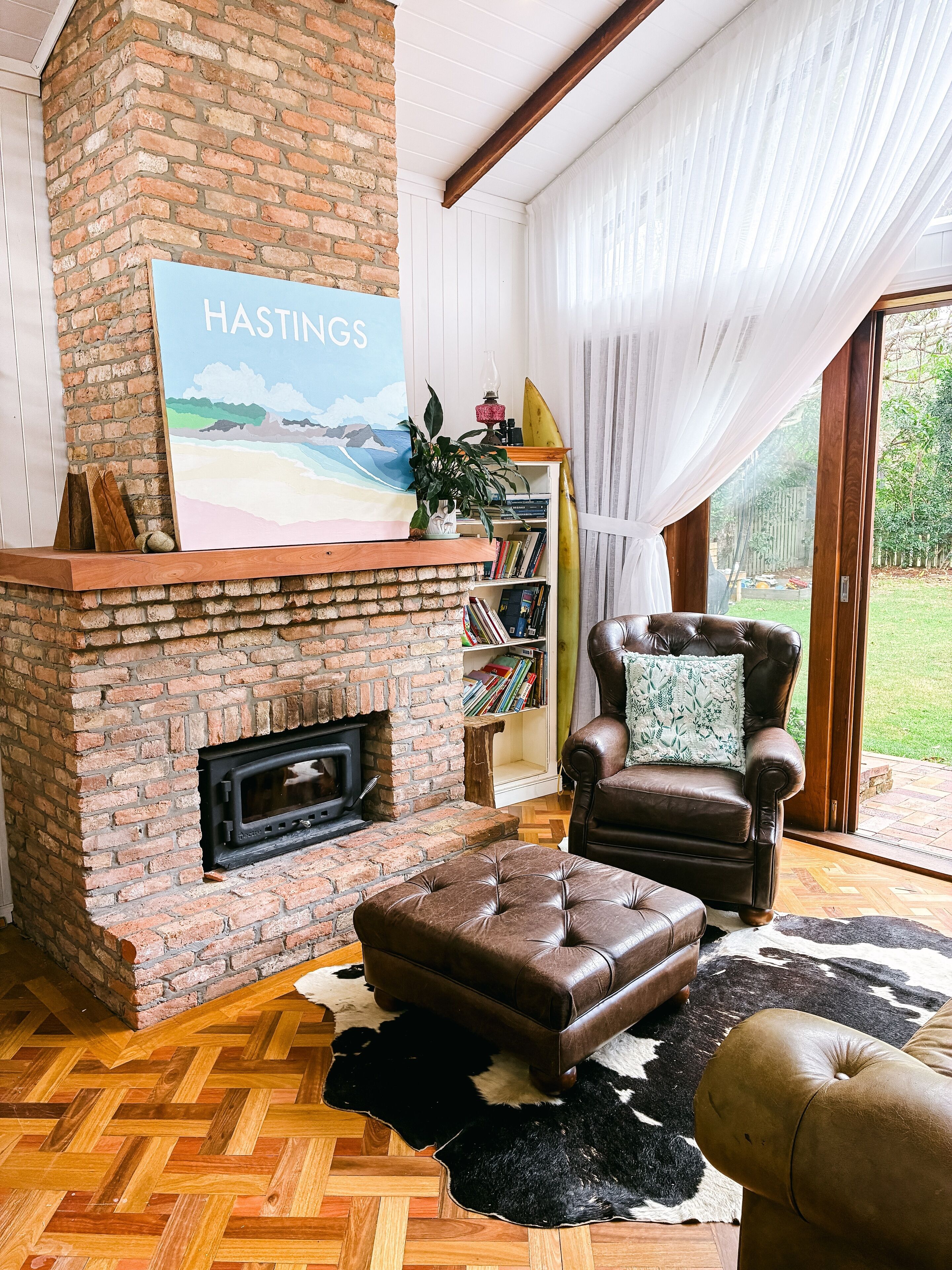 A cozy living room with a brick fireplace, a leather armchair, and a bookshelf.