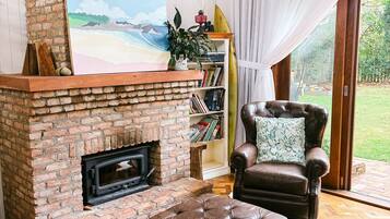 A cozy living room with a brick fireplace, a leather armchair, and a bookshelf.