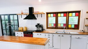 Une cuisine avec un plan de travail en bois, une cuisinière, une machine à café et une fenêtre aux vitraux colorés.
