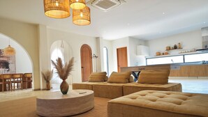 A modern living room with a sectional sofa, a round coffee table, and a dining area with wooden chairs. - MaShang Holiday Villas - Luxury 5BR Private Pool Villa in Jomtien (Muang Pattaya)