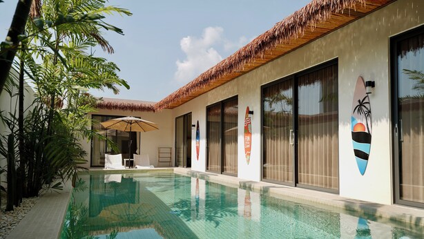 A swimming pool with a tiled edge, surrounded by a building with large windows and a thatched roof. - MaShang Holiday Villas - Luxury 5BR Private Pool Villa in Jomtien (Muang Pattaya)