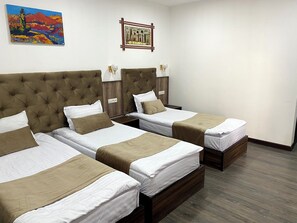 A hotel room with three beds, a large tufted headboard, bedside lamps, and a framed picture on the wall. - Art Grand  (Tashkent)