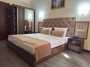 Un dormitorio con una cama grande, un armario de madera, mesitas de noche con lámparas y un cuadro en la pared.