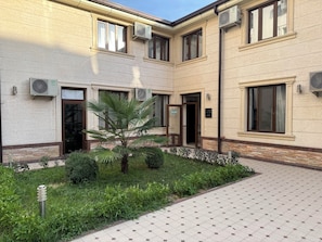 A building with multiple air conditioning units, a palm tree, and a paved entrance area. - Grand Art Premium Hotel (Tashkent)