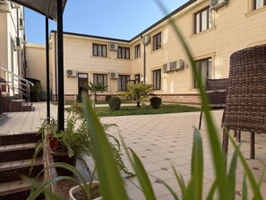 A courtyard with a building, steps, potted plants, and outdoor furniture. - Art Grand  (Tashkent)
