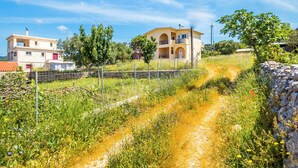 Zona residencial con un edificio de dos pisos, un sendero de tierra y vegetación circundante.