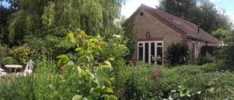 A single-story brick house with a sloped roof, surrounded by dense greenery and trees.
