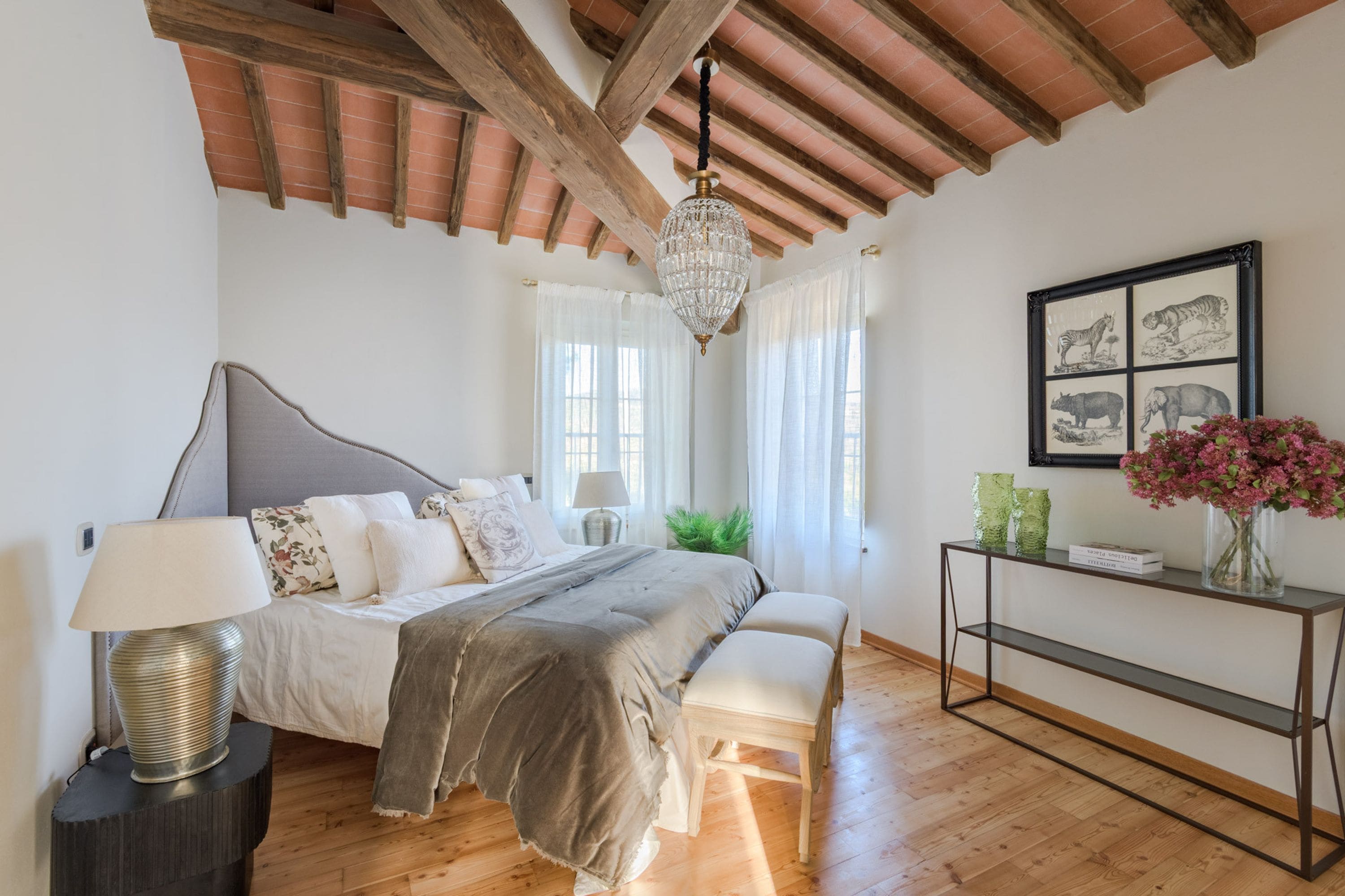 A bedroom with a bed, bedside table, lamp, bench, and a console table with decorative items.