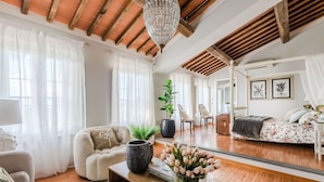 Un ampio soggiorno con soffitto in legno, un grande specchio, un divano, un tavolino da caffè con un vaso di fiori e un letto con biancheria da letto floreale.