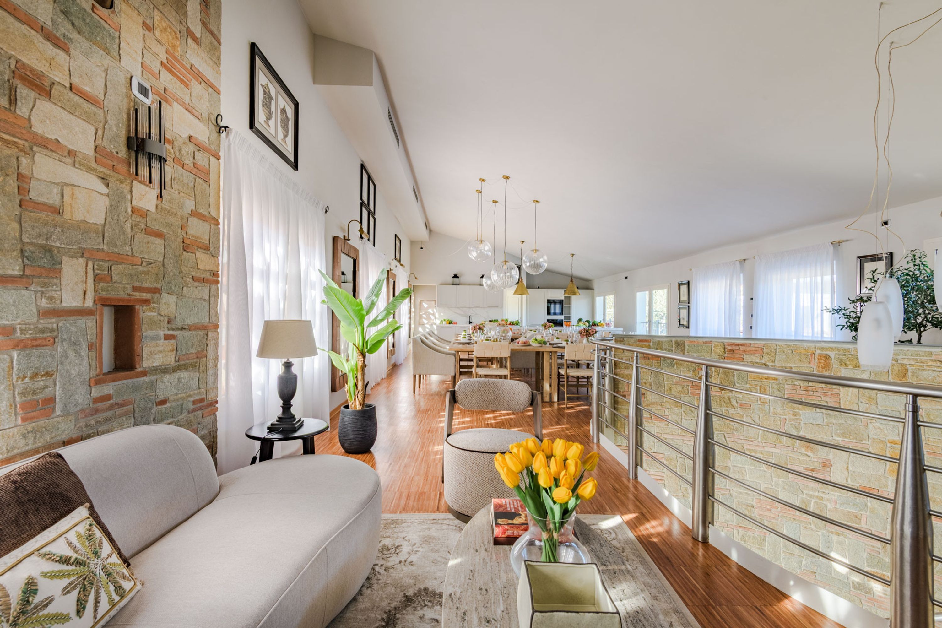 A spacious living area with a stone wall, a sofa, a coffee table with a vase of flowers, and a dining area in the background.