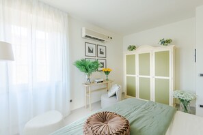 A bedroom with a bed, a bedside table with a lamp, a chair, a wardrobe, and a window with sheer curtains. - Corte Benedetto in Montecarlo (Capannori)