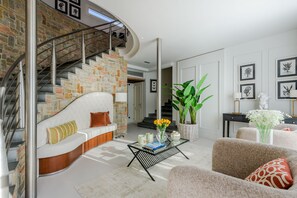 A modern living room with a curved staircase, a white sofa, a coffee table with books and flowers, and a large plant. - Corte Benedetto in Montecarlo (Capannori)