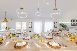 A spacious dining area with multiple tables set for a meal, clear glass pendant lights, and a view of the outdoors through large windows. - Corte Benedetto in Montecarlo (Capannori)