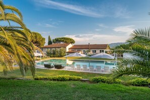 A pool area with lounge chairs and umbrellas, surrounded by greenery and buildings. - Corte Benedetto in Montecarlo (Capannori)