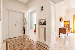 Vestíbulo de hotel con suelo de baldosas, un mostrador de recepción, perchero, planta y señalización de salida de emergencia.