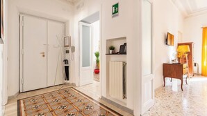 A hotel lobby with a tiled floor, a reception desk, a coat rack, a plant, and a sign indicating an emergency exit. - Rhome Elegant Apartment (Roma)