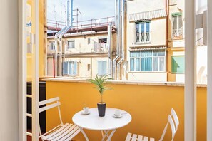 A balcony with a small table and chairs, a potted plant, and a view of neighboring buildings. - Rhome Elegant Apartment (Roma)