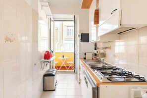 A narrow kitchen with white tiles, a gas stove, a small trash bin, and a red bag on the counter. - Rhome Elegant Apartment (Roma)