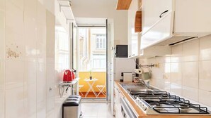 A narrow kitchen with white tiles, a gas stove, a small trash bin, and a red bag on the counter. - Rhome Elegant Apartment (Roma)