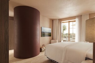Habitación de hotel con una cama grande, una ventana con cortinas, un cuadro en la pared y un pilar de madera.