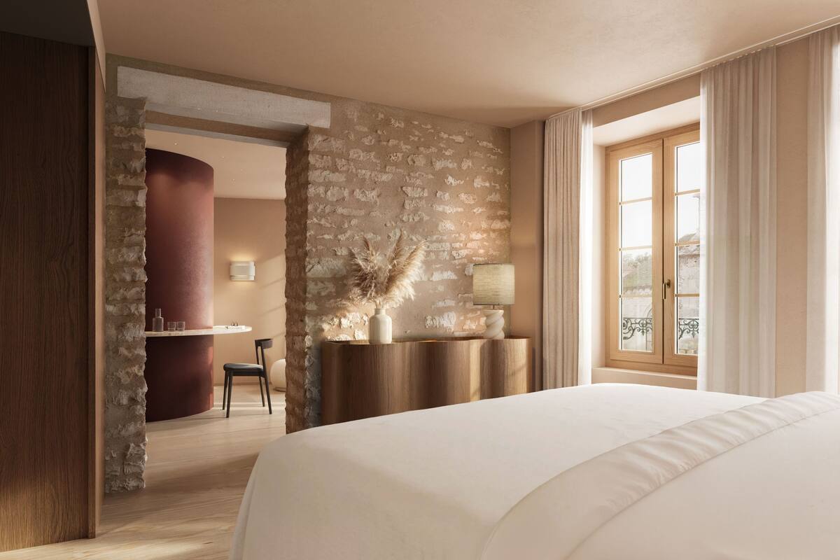 A hotel room with a large bed, a stone wall, a wooden desk, and a window with curtains.