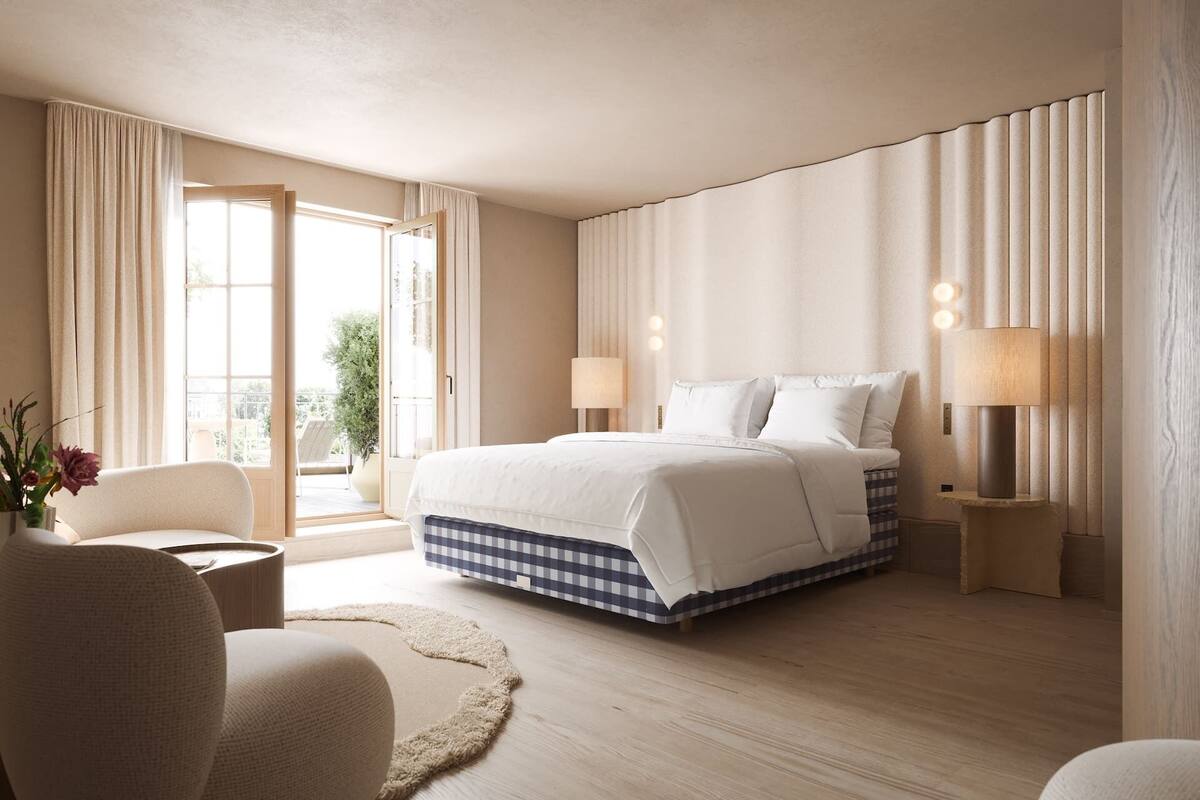 A hotel room with a large bed, two bedside lamps, a view through a glass door, and a small seating area with a chair and a table.