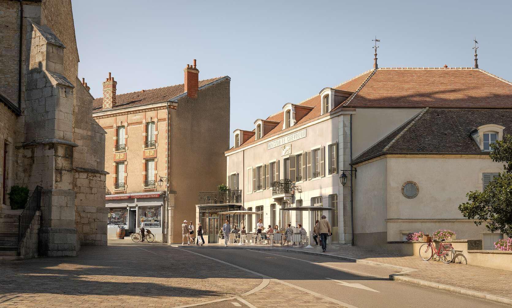 Une rue bordée d’immeubles, dont un café doté d’une terrasse et d’une enseigne indiquant « Cafétéria et bar ».