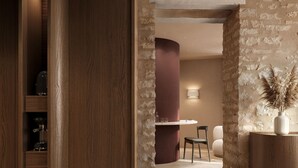 Un interior moderno con una escalera de madera, una pared de piedra y una zona de estar con un jarrón de plantas secas.