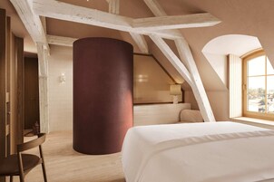 Un dormitorio con una cama grande, una silla de madera, un alto pilar y una ventana con vistas.